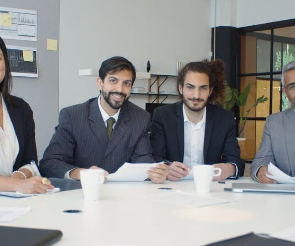 A diverse group of business professionals having a meeting in a modern office setting, engaged and smiling.