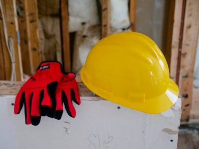 Close-up of a yellow hard hat and red gloves on a construction site, symbolizing safety and work.